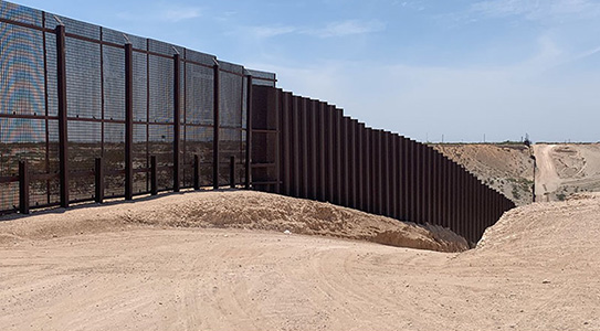 metal grated border wall in the middle of the desert
