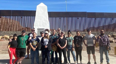 Photo of a group gathered for a photo with the border wall in the background in Ciudad Juárez, Mexico 