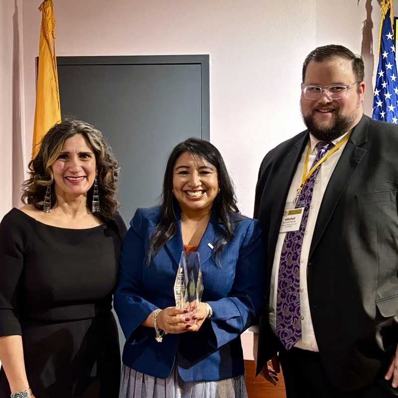 Three people standing with one holding an award